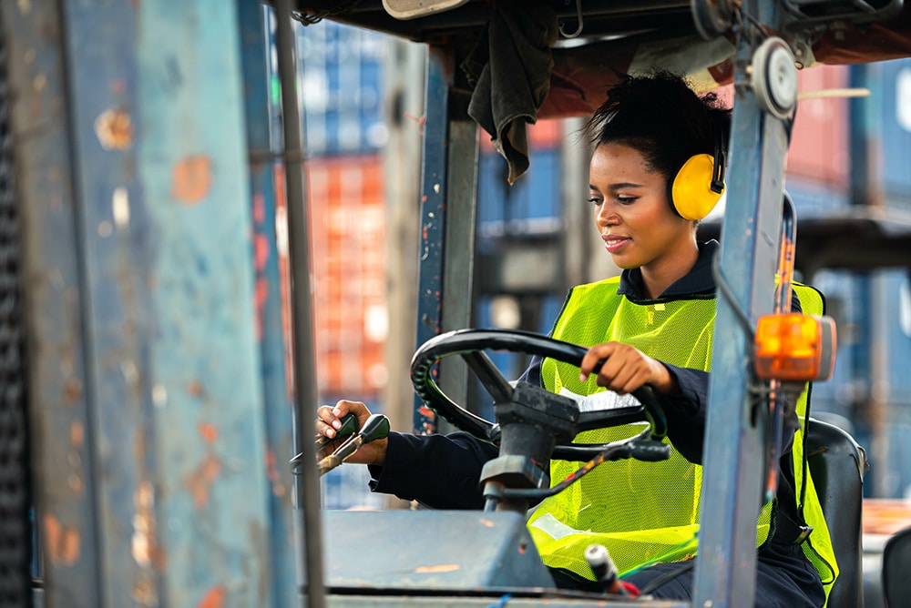 Female worker driving forklift in industrial container warehouse
